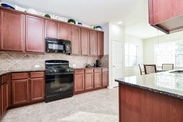 a kitchen with stainless steel appliances granite countertop a stove top oven a sink dishwasher a dining table and chairs with wooden floor