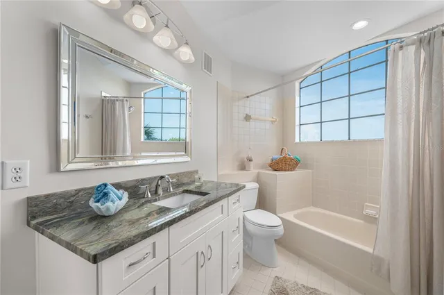 a bathroom with a granite countertop sink a toilet a mirror and bathtub