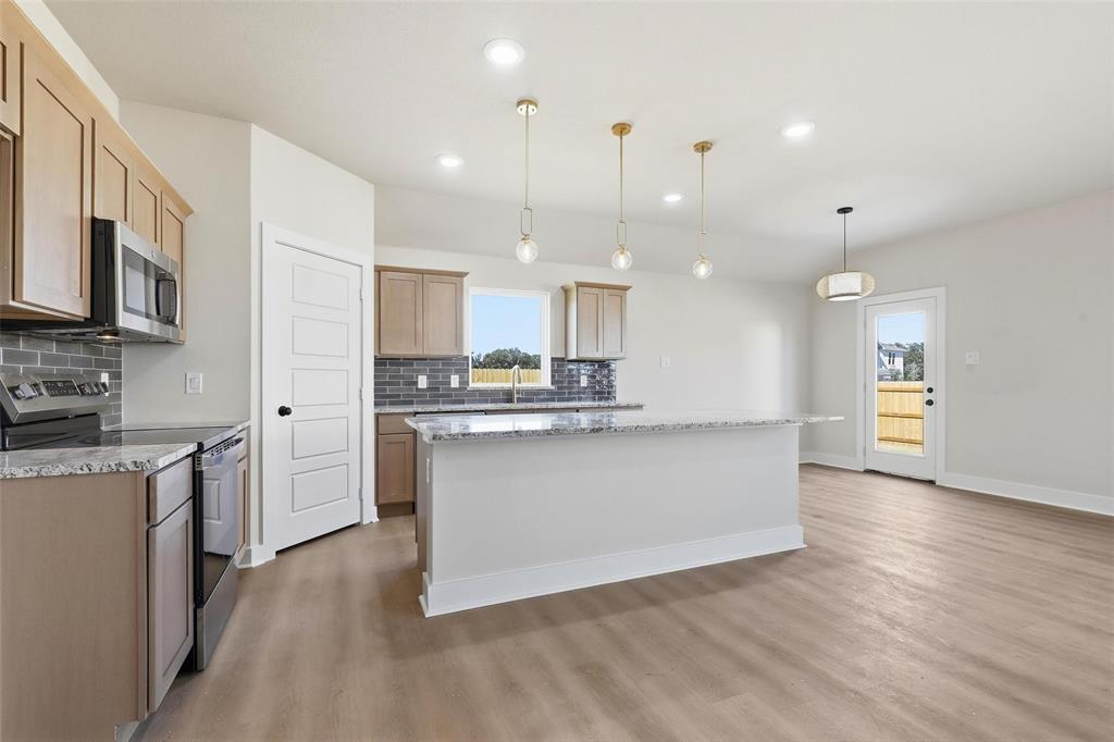 472 Peace Lily Way Tolar, TX 76476 - Photo 6 of 40 a large kitchen with stainless steel appliances granite countertop a sink a stove a refrigerator a center island and a wooden floor