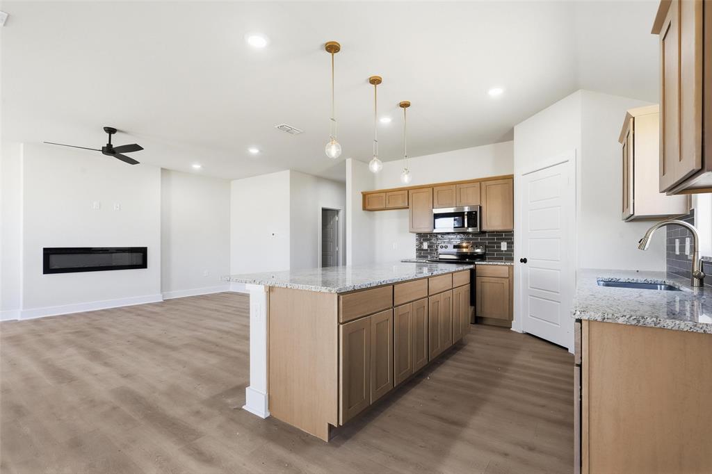 472 Peace Lily Way Tolar, TX 76476 - Photo 9 of 40 a kitchen with stainless steel appliances kitchen island granite countertop a refrigerator oven a sink dishwasher and white cabinets with wooden floor