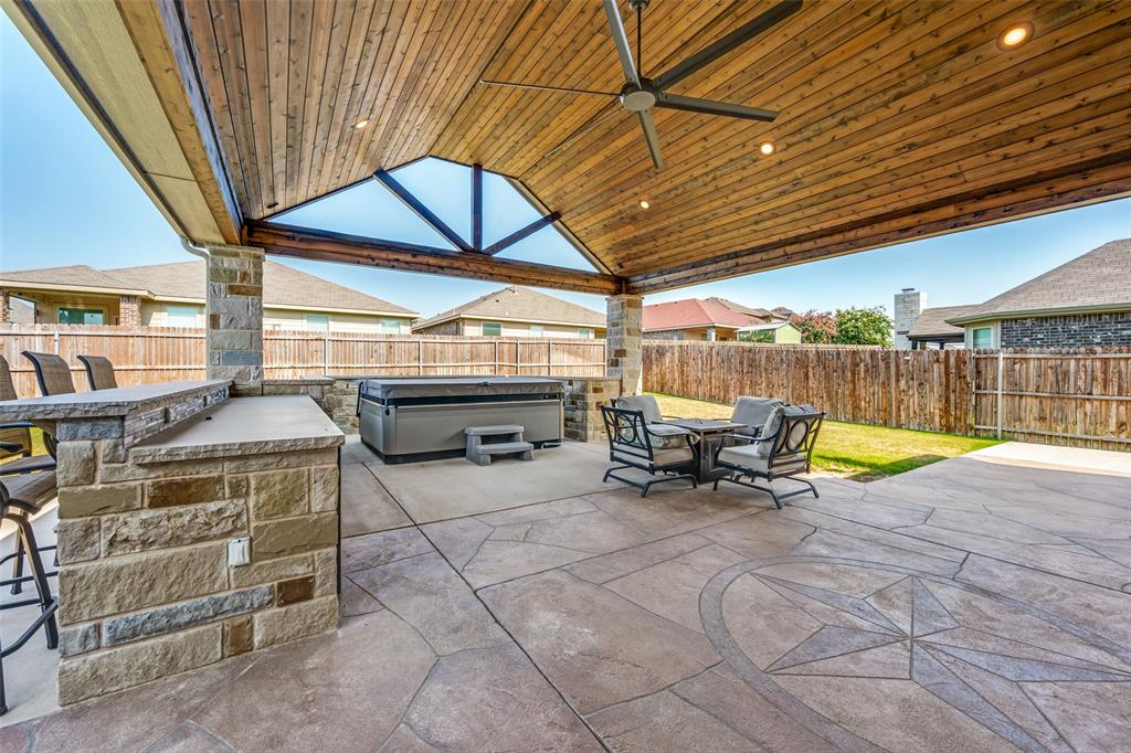 15725 Preble Road Fort Worth, TX 76177 - Photo 23 of 25 Expansive covered patio featuring a wood-finish ceiling with integrated lighting, stone fireplace with built-in seating ledge, and stamped concrete flooring