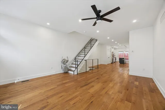 an empty room with wooden floor a ceiling fan and staircase