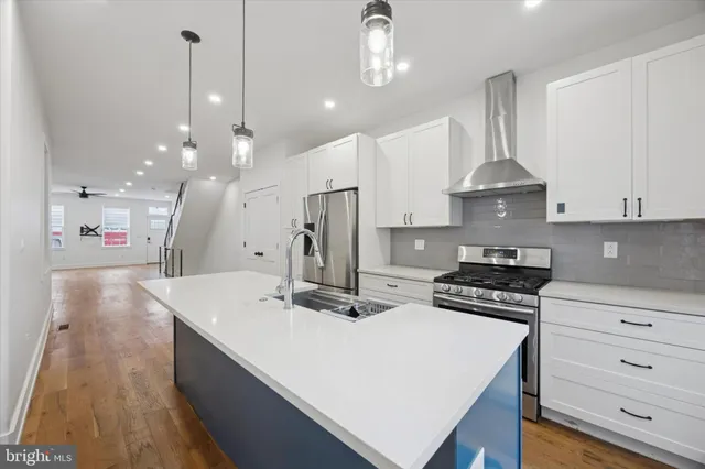 a kitchen with stainless steel appliances a stove a sink a refrigerator and white cabinets with wooden floor