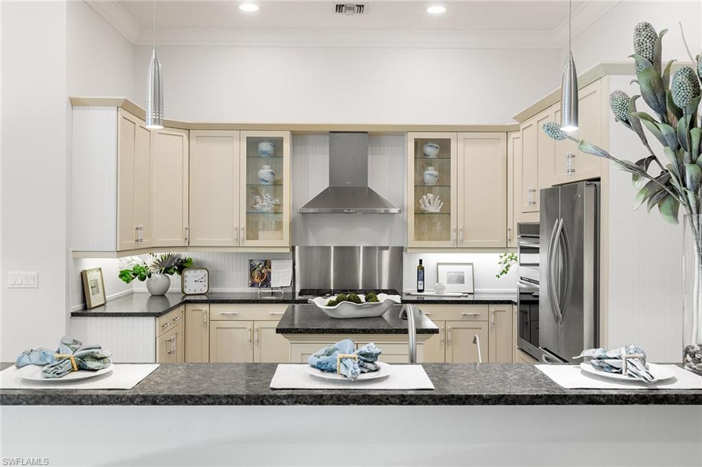 642 Bougainvillea Road Naples, FL 34102 - Photo 16 of 50 Kitchen with decorative light fixtures, wall chimney exhaust hood, cream cabinets, stainless steel appliances, and crown molding