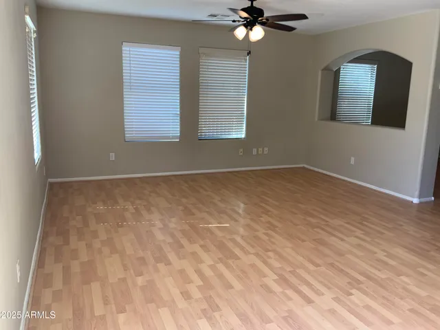 a view of an empty room with wooden floor and a chandelier fan