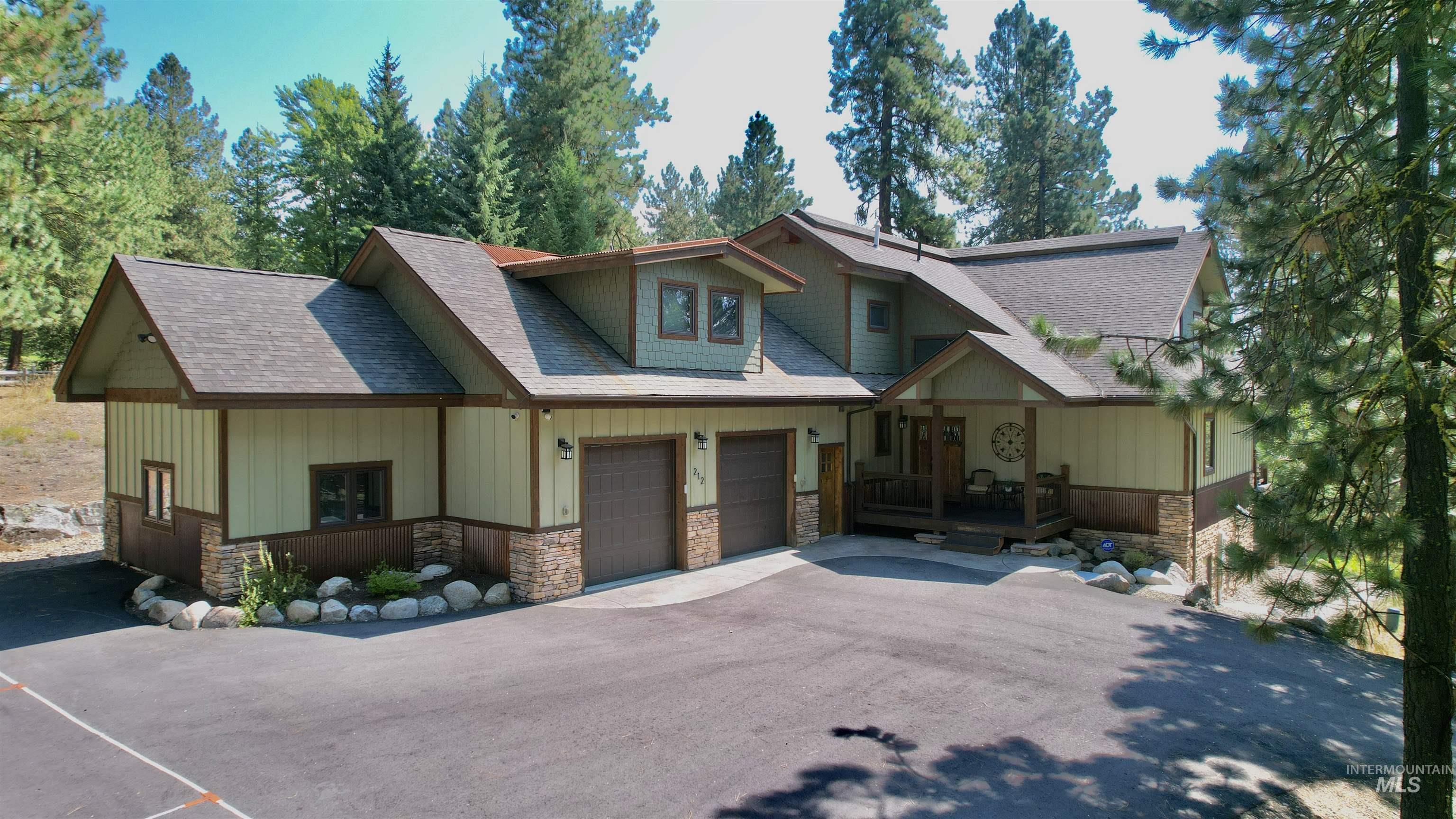 View of front of house featuring stone siding, roof with shingles, a garage, driveway, and board and batten siding