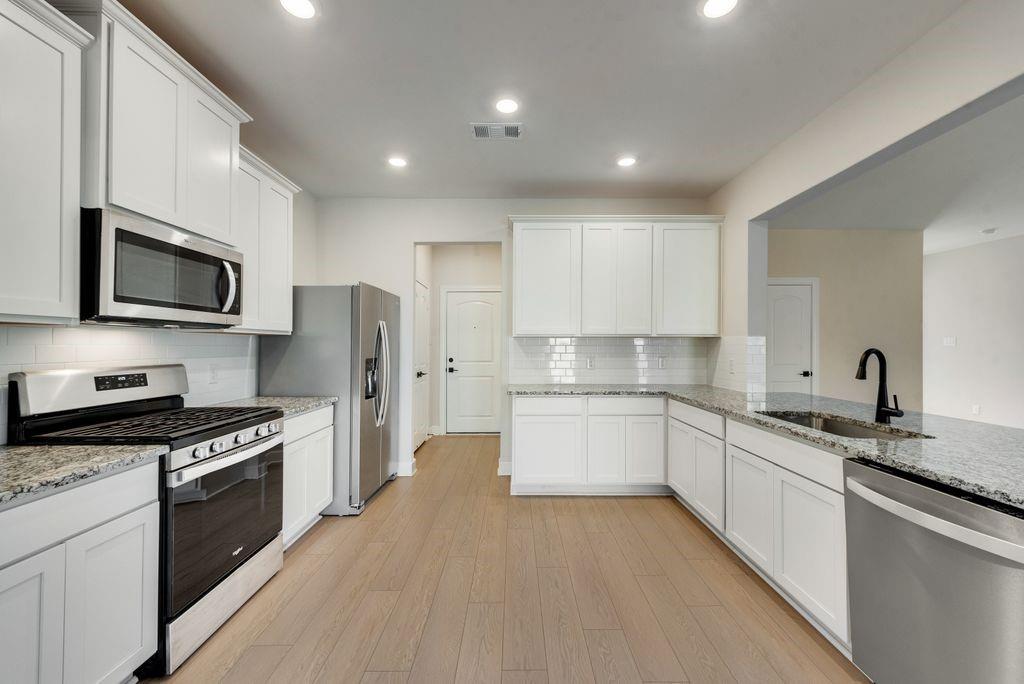1421 Butler Avenue Princeton, TX 75407 - Photo 10 of 25 a large kitchen with stainless steel appliances granite countertop a stove top oven a sink dishwasher a refrigerator and white cabinets with wooden floor