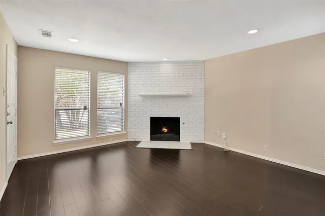 a view of an empty room with wooden floor fireplace and a window