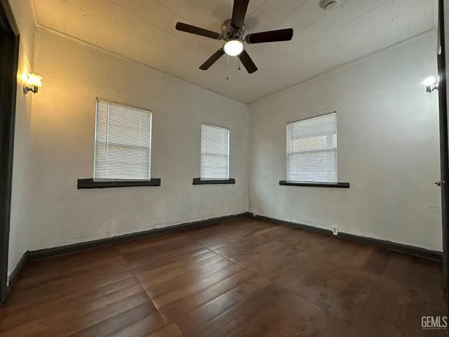 an empty room with wooden floor fan and windows