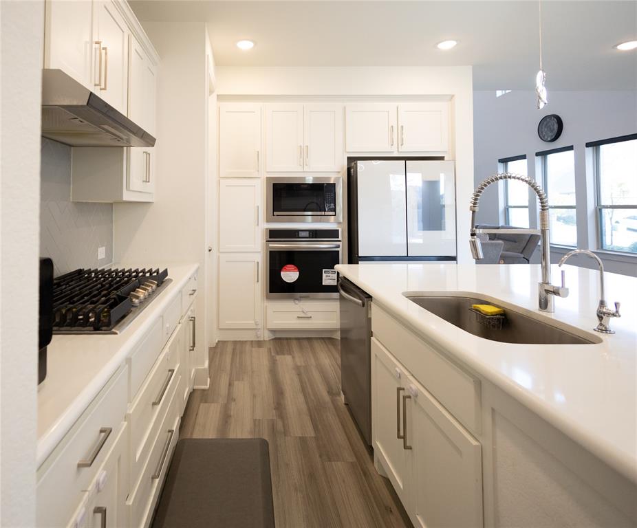 3017 Andorra Road McKinney, TX 75071 - Photo 13 of 40 Modern galley kitchen featuring white cabinetry with chrome hardware, wood-finish flooring, quartz countertops, dual stainless steel ovens, gas cooktop, stainless steel refrigerator with ice dispenser, and an oversized apron-front sink with contemporary arc faucet