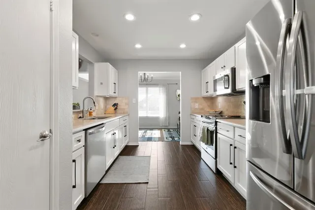 a large kitchen with stainless steel appliances sink a stove and white cabinets