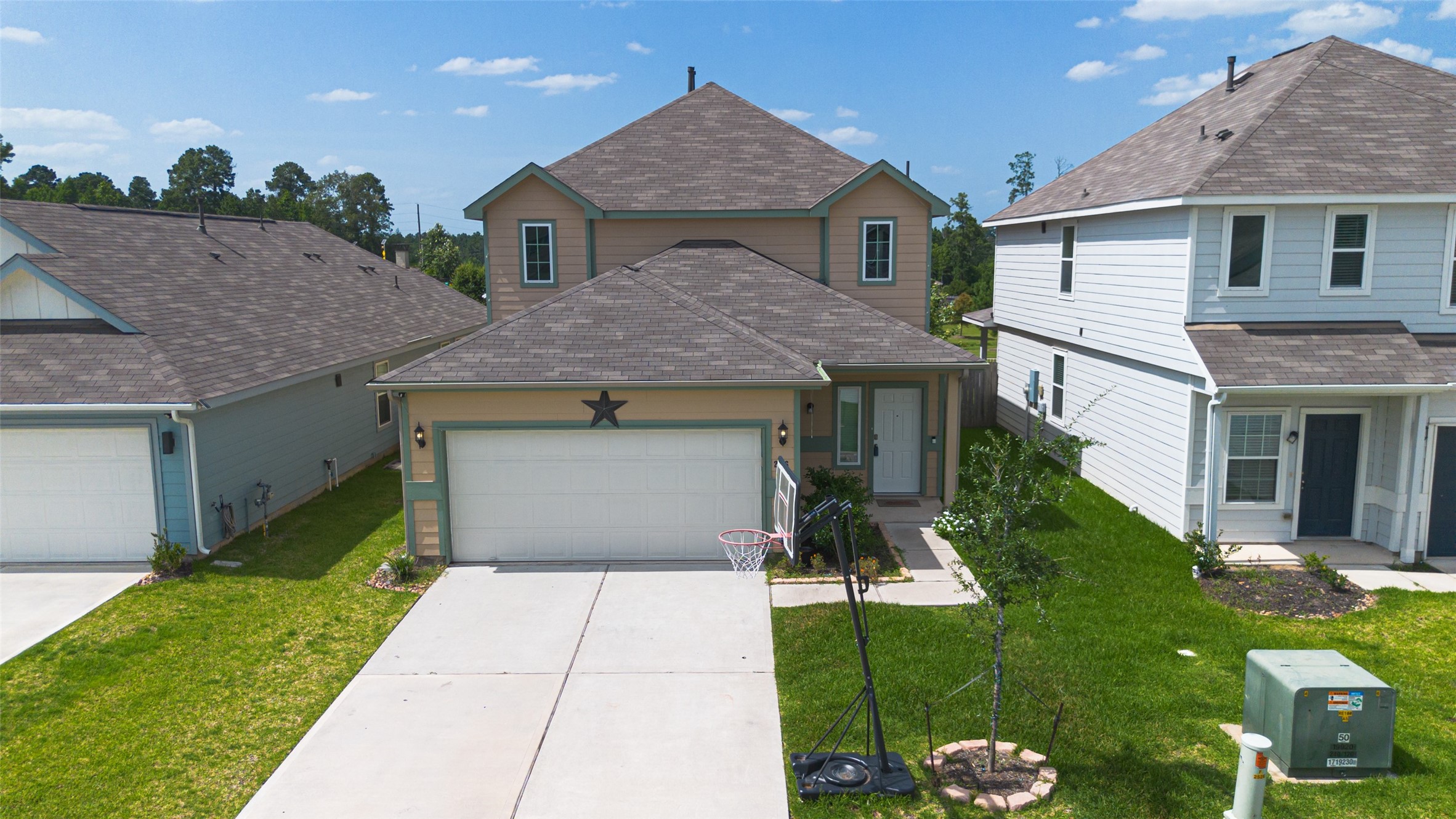 2526 Sturgeon Way Conroe, TX 77384 - Photo 44 of 49 This photo showcases a two-story house with a neatly maintained front yard and driveway. The home features a two-car garage and a charming façade with a decorative star. It is situated in a residential neighborhood with nearby houses and a backdrop of trees, offering a suburban feel.