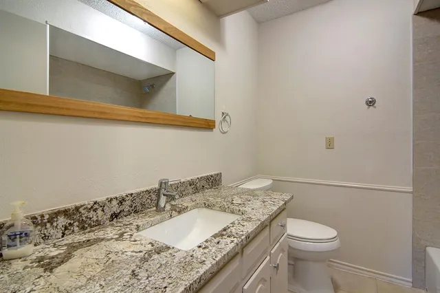 a bathroom with a granite countertop sink a toilet and mirror
