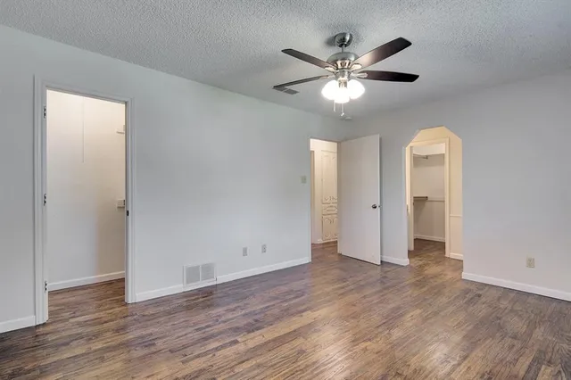 a view of an empty room with wooden floor and a ceiling fan