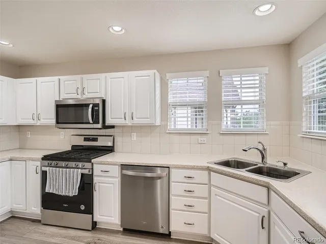 a kitchen with white cabinets appliances a sink and a window