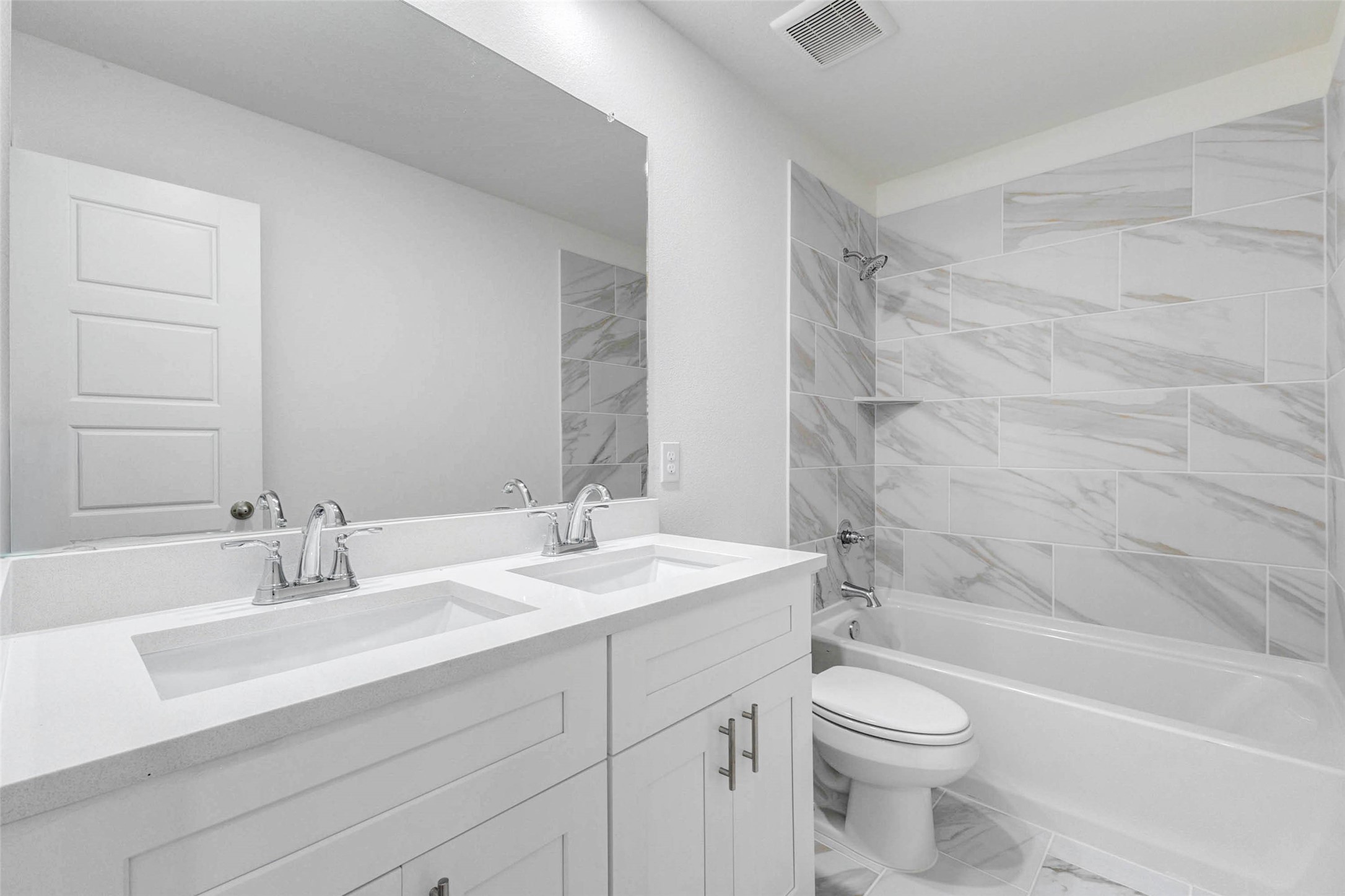 6463 Escondido Drive Rosharon, TX 77583 - Photo 14 of 30 Secondary bathroom featuring a bright double-sink vanity, white cabinetry, chrome fixtures, large mirror, and a tub/shower combo with marble-look tile surround. The clean neutral finishes create a polished, modern look while offering everyday functionality for guests or secondary bedrooms.
