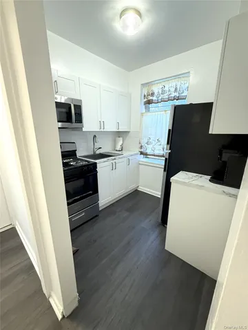 a kitchen with granite countertop a refrigerator stove a sink and white cabinets with wooden floor