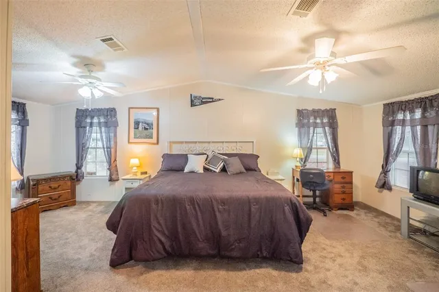a spacious bedroom with a bed a mirror on dresser and a chandelier