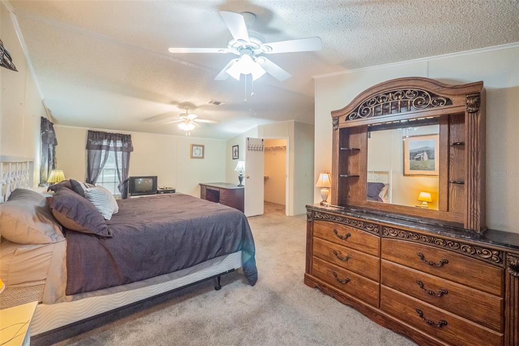 37510 Quail Ridge Circle Leesburg, FL 34788 - Photo 22 of 43 a spacious bedroom with a bed a mirror on dresser and a chandelier