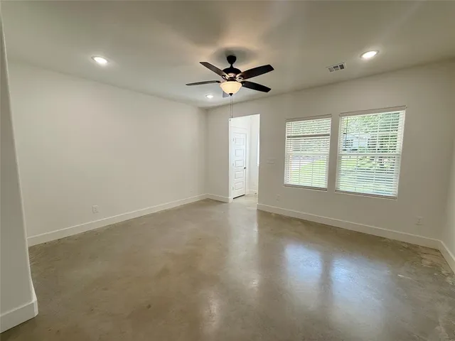 an empty room with wooden floor ceiling fan and windows