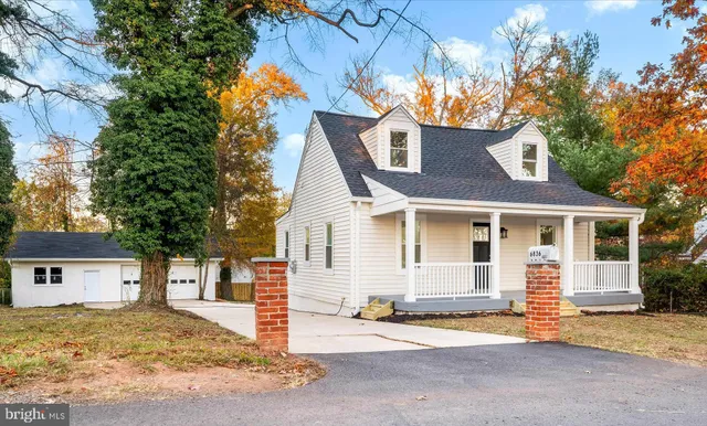 a view of a white house with large tree and wooden fence