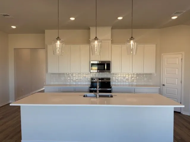 a large kitchen with stainless steel appliances granite countertop a large counter top a wooden floors and a large window