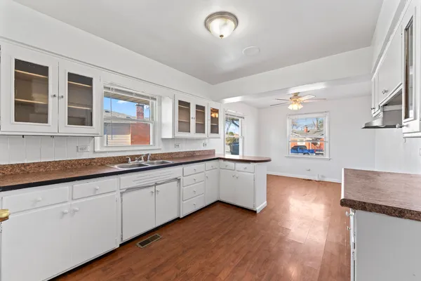 a large white kitchen with granite countertop a sink and dishwasher cabinets with wooden floor