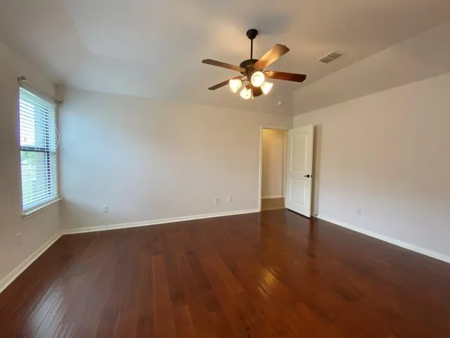 an empty room with wooden floor fan and windows