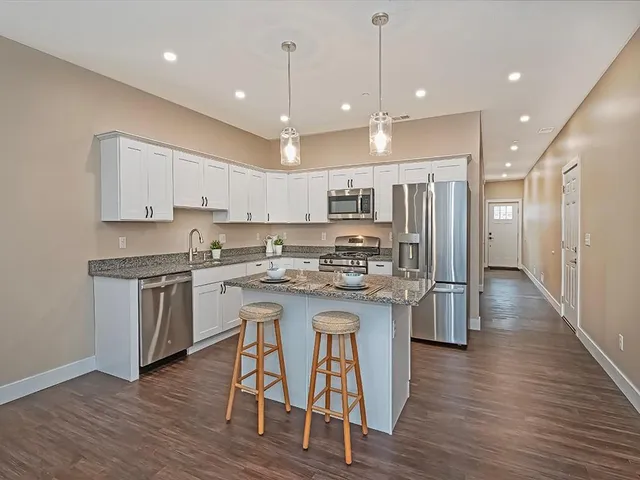 a kitchen with stainless steel appliances granite countertop a table chairs stove a sink dishwasher a refrigerator and cabinets with wooden floor