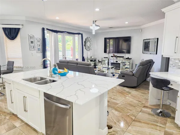 a large kitchen with kitchen island a sink a counter top space and a view of living room