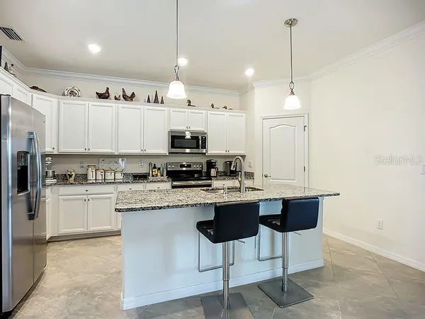 a kitchen with stainless steel appliances granite countertop a sink a stove a refrigerator and white cabinets with wooden floor