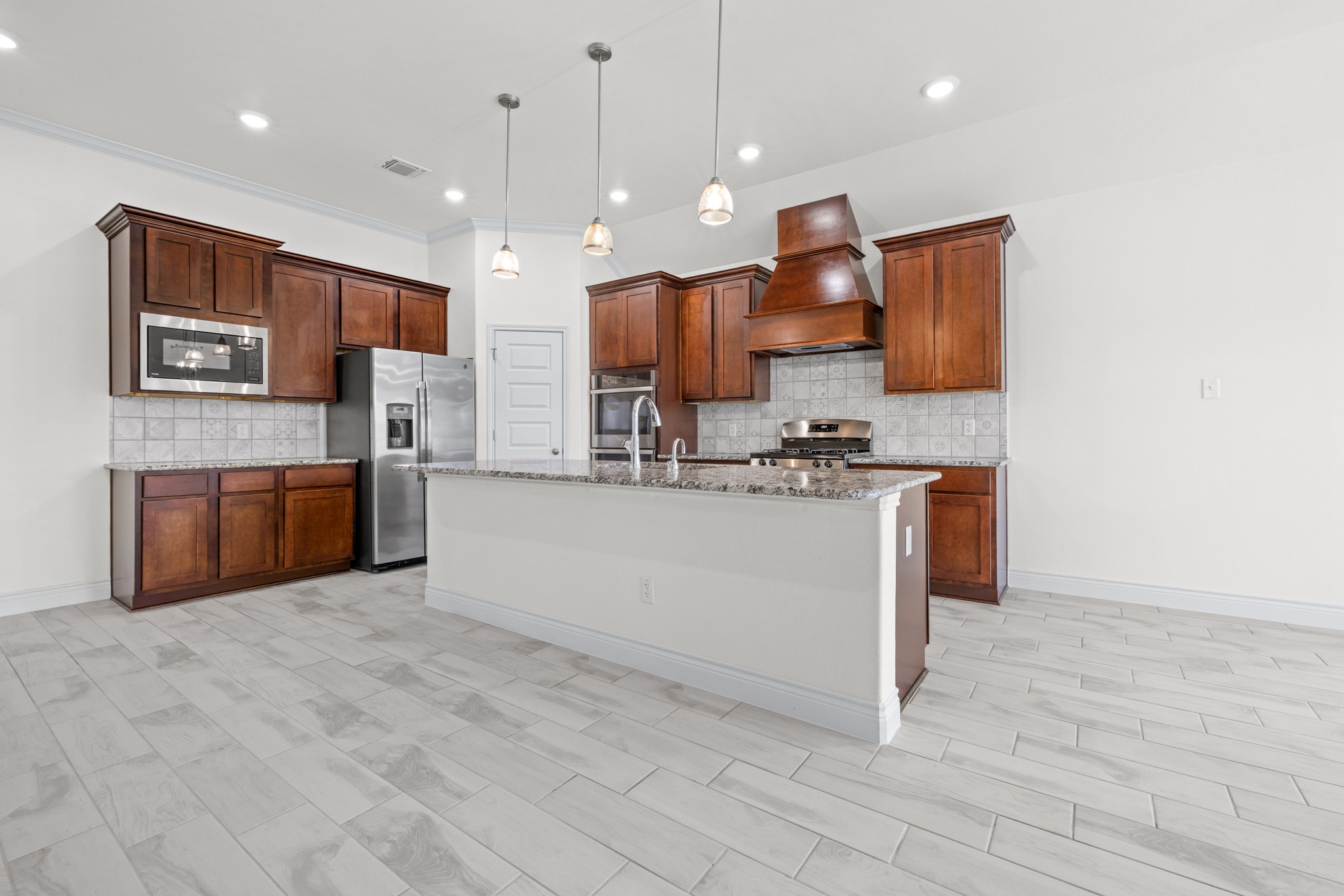 6019 Monza Drive Temple, TX 76502 - Photo 11 of 40 Kitchen featuring light stone counters, stainless steel appliances, tasteful backsplash, a kitchen island with sink, and crown molding