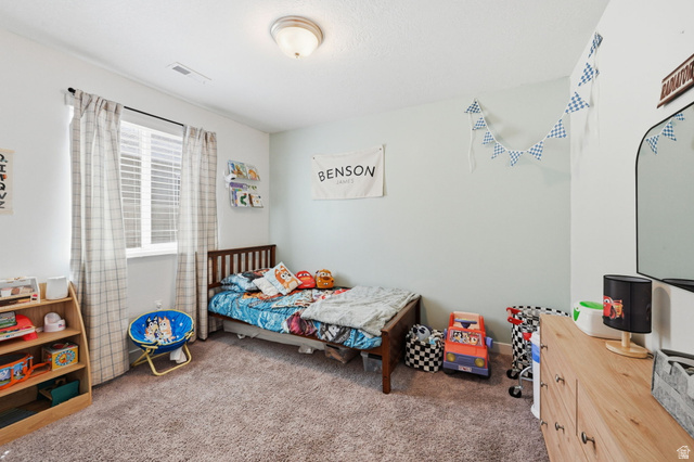 1175 Silver Hollow Road Syracuse, UT 84075 - Photo 22 of 34 Carpeted bedroom featuring a window with blinds and curtains, light blue wall accent, and a flush mount ceiling light fixture