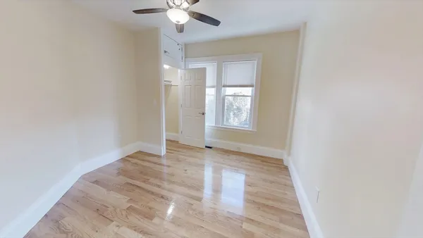 an empty room with wooden floor chandelier fan and windows