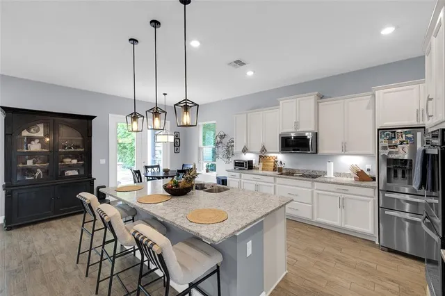 a open kitchen with stainless steel appliances granite countertop a sink a stove a kitchen island with chairs and wooden floor