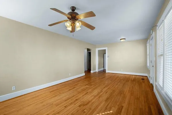 an empty room with wooden floor chandelier fan and windows
