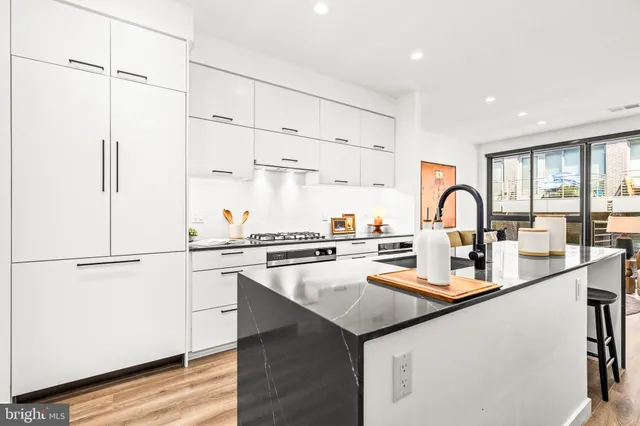 a kitchen with stainless steel appliances a sink a stove and white cabinets with wooden floor