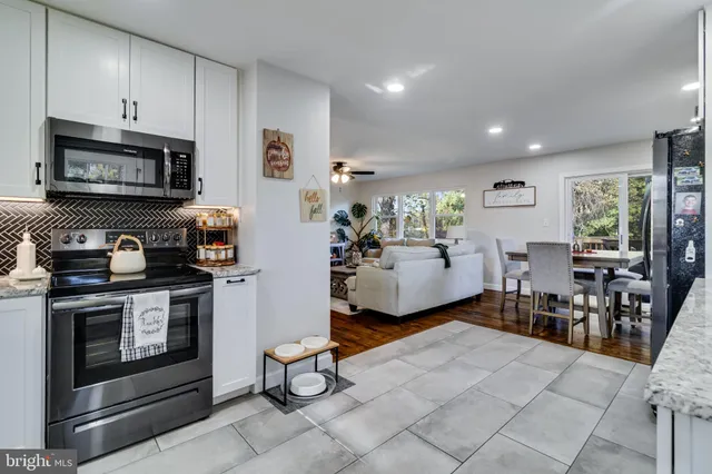 a living room with stainless steel appliances furniture a fireplace a flat screen tv and a window