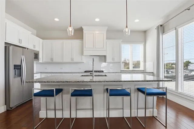 a kitchen with granite countertop a stove a refrigerator and white cabinets with wooden floor