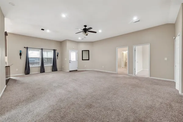 a view of an empty room with chandelier fan and windows