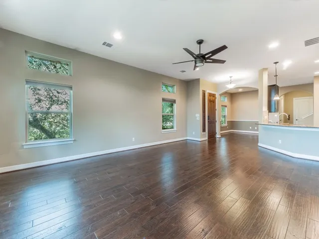 an empty room with wooden floor a ceiling fan and kitchen view
