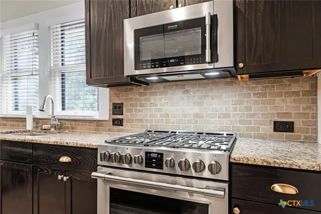 a kitchen with granite countertop a stove top oven cabinetry a sink and a window