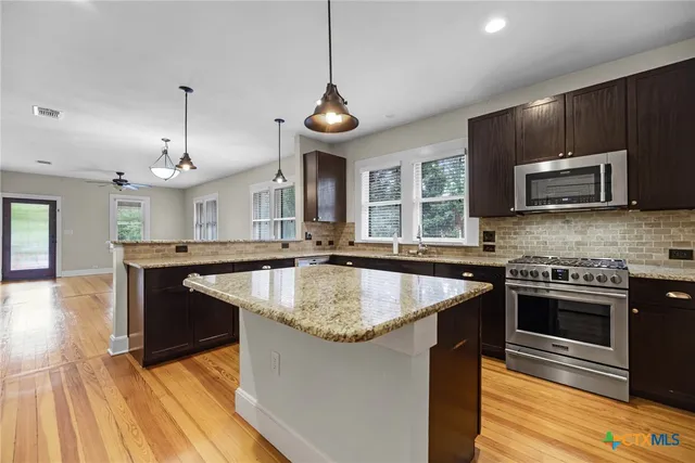 a kitchen with stainless steel appliances granite countertop a sink a stove and a wooden floors