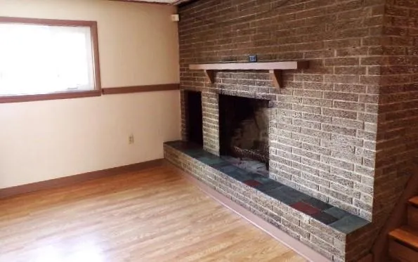 a view of an empty room with wooden floor and a fireplace