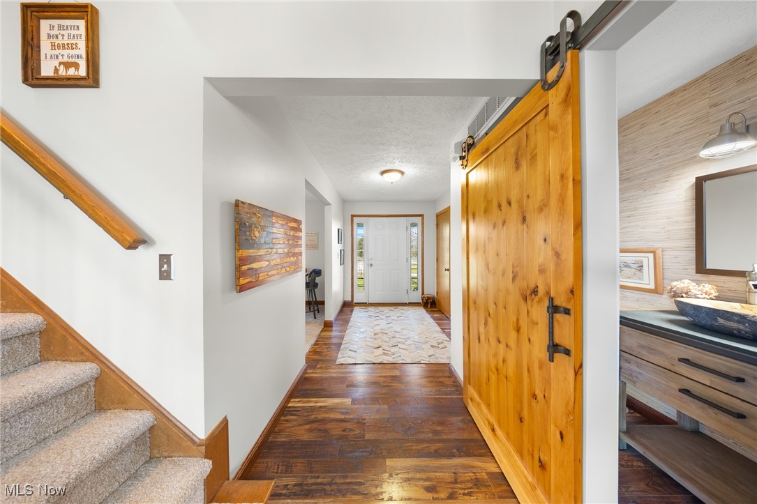 Hall with baseboards, stairway, a barn door, a textured ceiling, and dark wood-style flooring