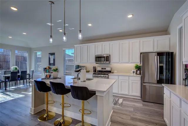 a kitchen with stainless steel appliances kitchen island granite countertop a refrigerator a stove a sink a dining table and chairs with wooden floor