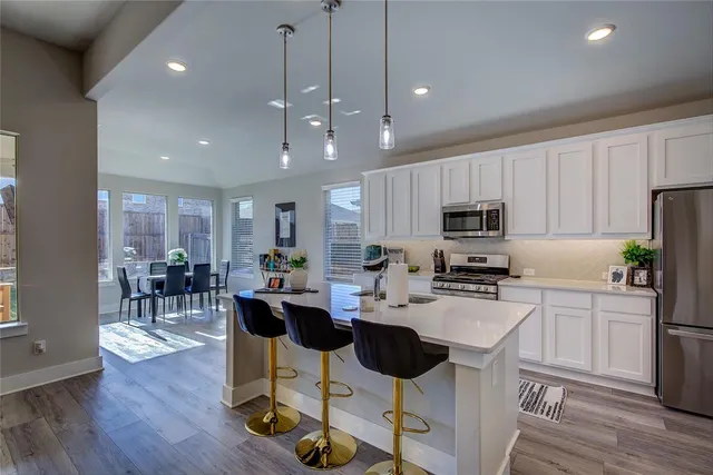 a kitchen with stainless steel appliances kitchen island granite countertop a stove a refrigerator a sink a dining table and chairs with wooden floor