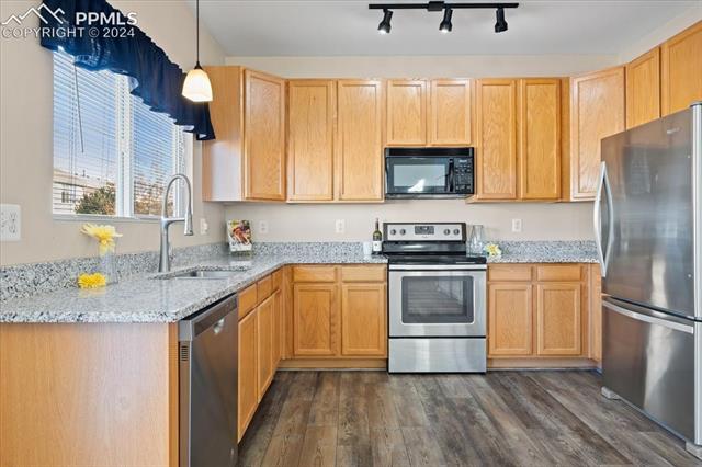 7655 Coffee Road Peyton, CO 80831 - Photo 7 of 31 Kitchen with light stone countertops, sink, LVP flooring, pendant lighting, and appliances with stainless steel finishes