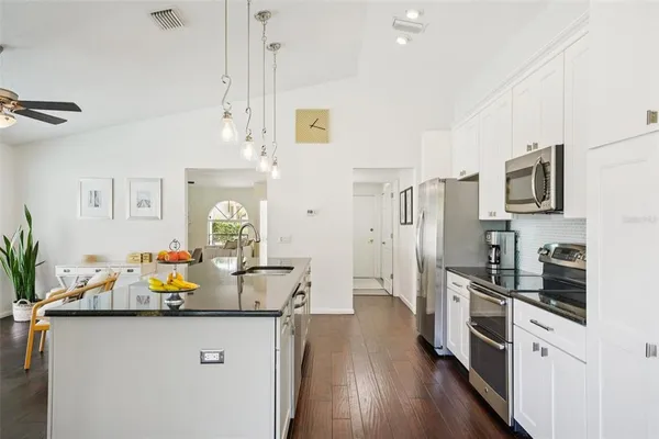 a kitchen with stainless steel appliances granite countertop a refrigerator a sink dishwasher a dining table and chairs with wooden floor