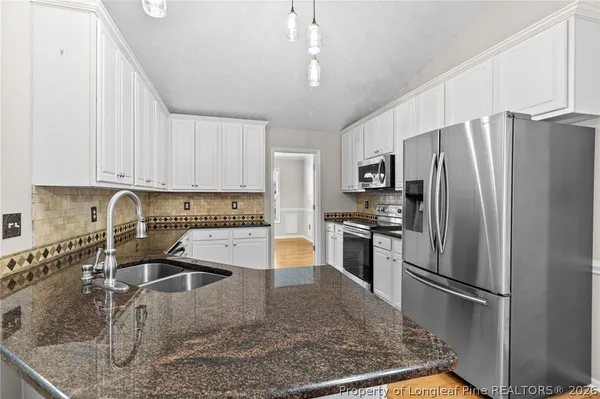 a kitchen with stainless steel appliances granite countertop a refrigerator a stove a sink a stove with white cabinets